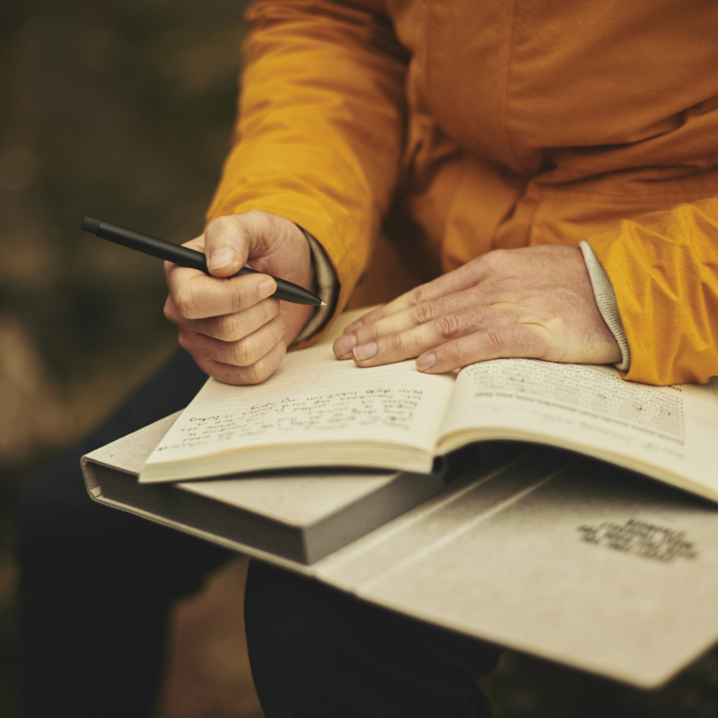A man is holding a pen and diary in hand and writing something