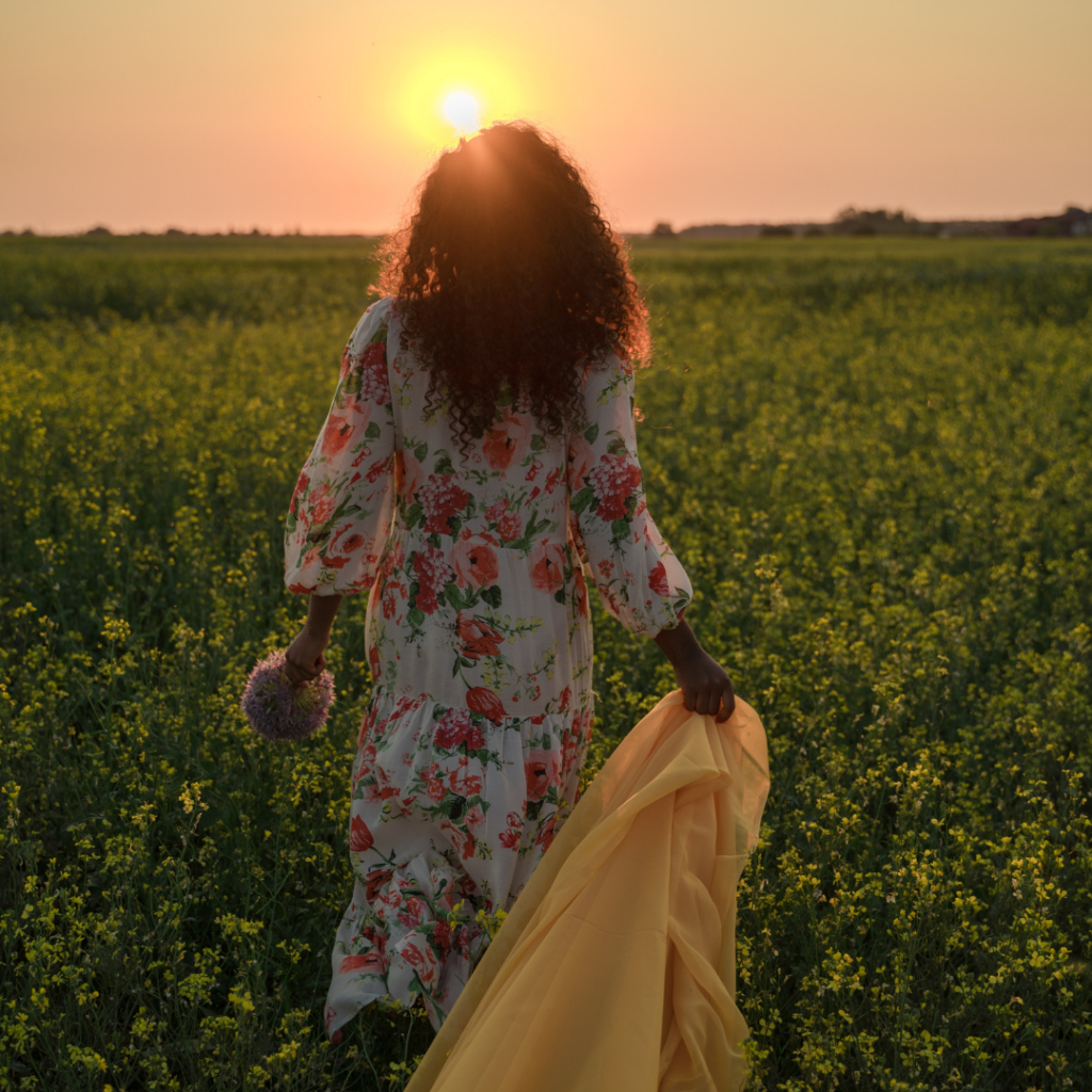 women in a sunflower field  in the evening, having  a flower in one hand and scarf in another 