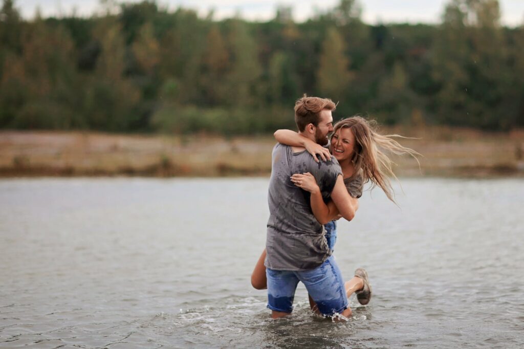 man hugging laughing woman while standing in body of water