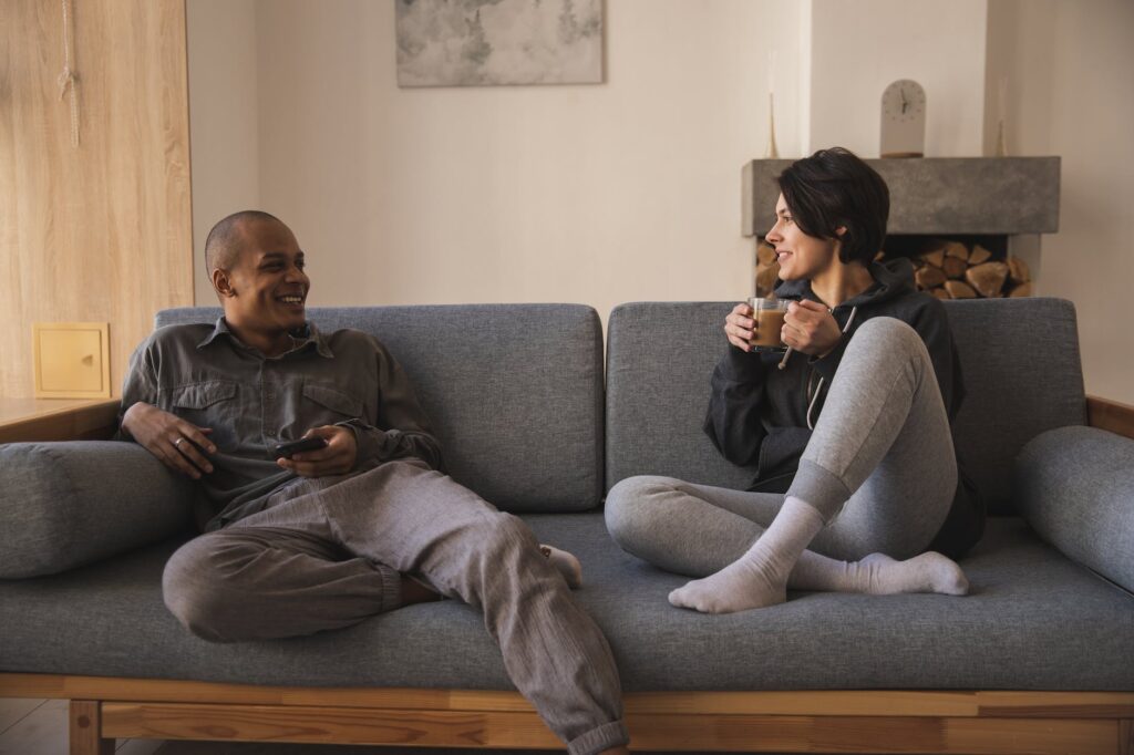 happy young multiracial couple talking on sofa at home