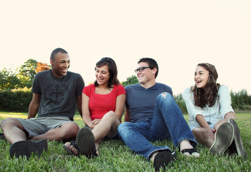 smiling women and men sitting on green grass with their friends
