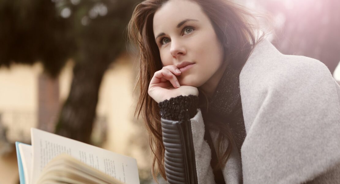 pensive woman in gray coat holding book