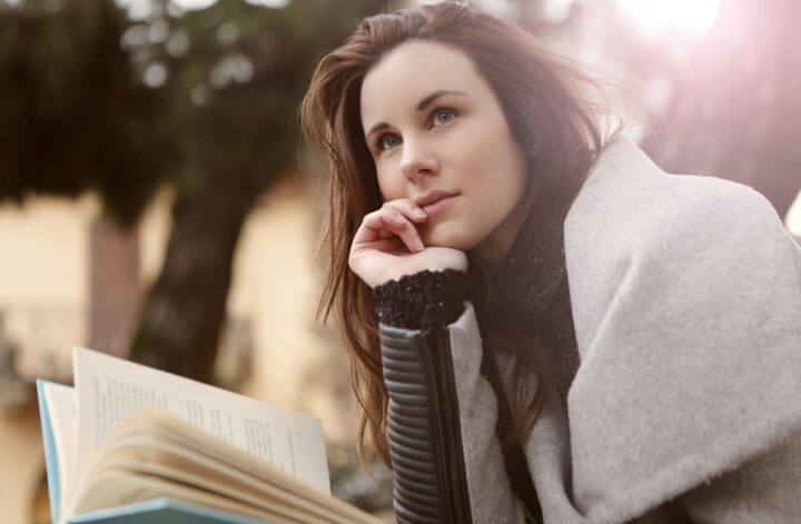 pensive woman in gray coat holding book